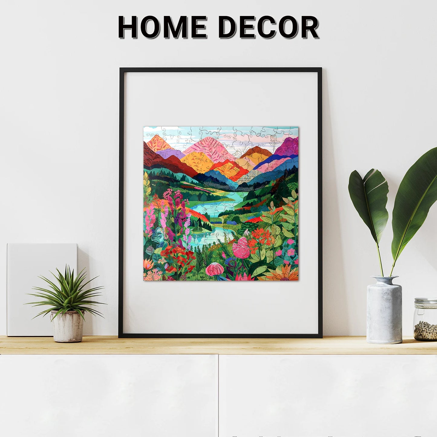 Framed colorful landscape artwork displayed on a wooden shelf alongside plants and a lycheepuzzles Mountain Abstract Wooden Jigsaw Puzzle for Adults with 200 pieces, under the text "HOME DECOR.