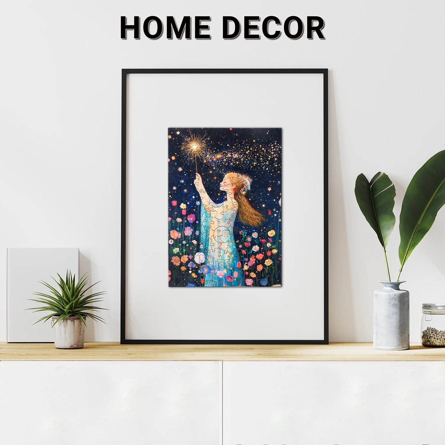 A framed artwork of a person surrounded by stars and flowers sits on a shelf with plants, decor, and the lycheepuzzles Magic Fairy Wooden Jigsaw Puzzle for Adult Kids Gifts (200 Pieces), featuring unique shapes, adding charm and intrigue.