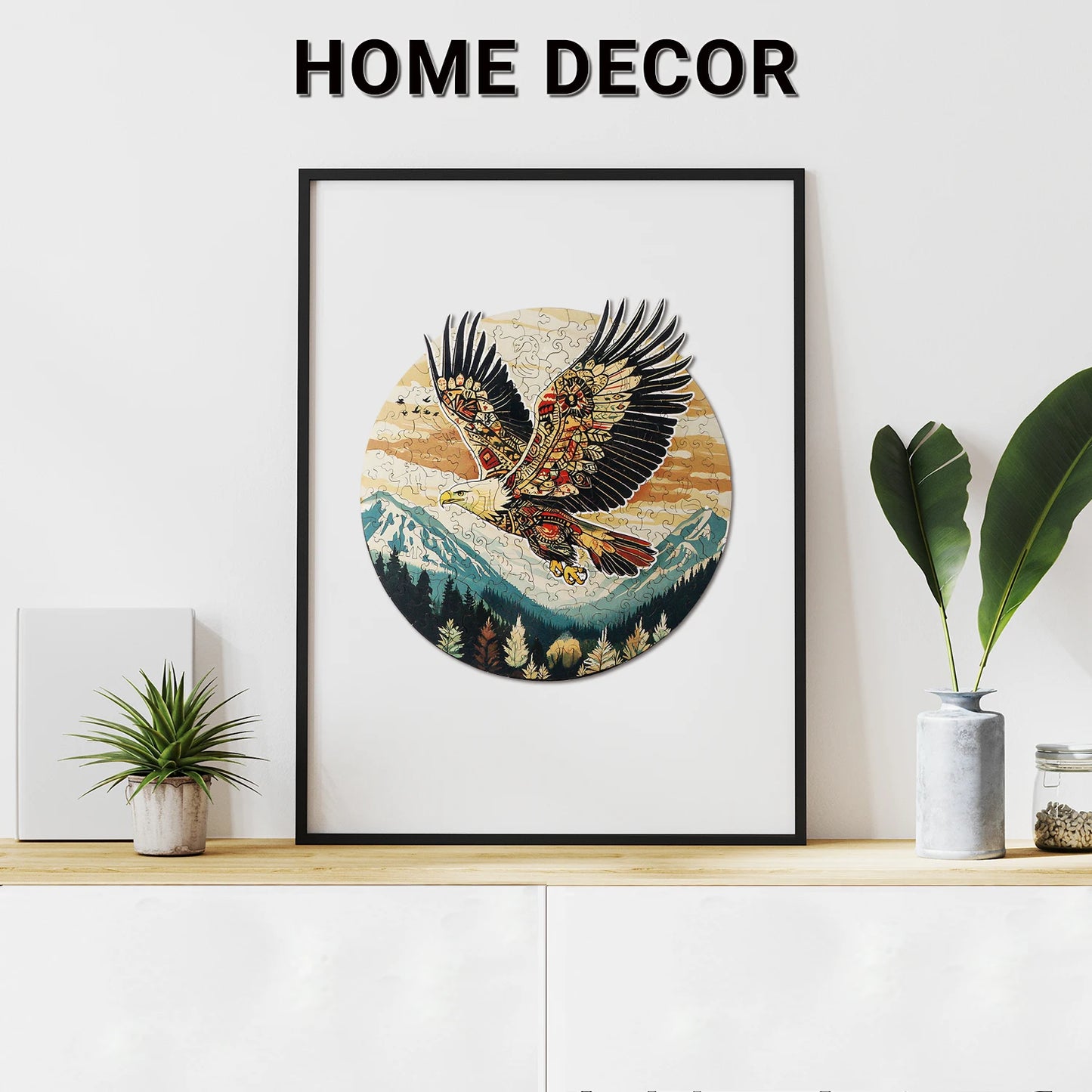 A framed image of an eagle soaring through a mountain landscape hangs above a cabinet decorated with a potted plant, accompanied by "Home Decor" and the Lycheepuzzles 200pcs Eagle Wooden Jigsaw Puzzle for Adults, known for its precision-cut pieces that add sophistication.