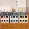 A single lycheepuzzles 1:12 Dollhouse Miniature Wooden Little House with a blue roof is showcased on a wooden surface, emphasizing its detailed construction. In the background, there's a white sofa and cabinet, enhancing the overall appeal.